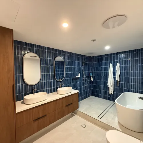 Bathroom renovation with a freestanding oval bath, dual backlit oval mirrors and navy feature tiling
