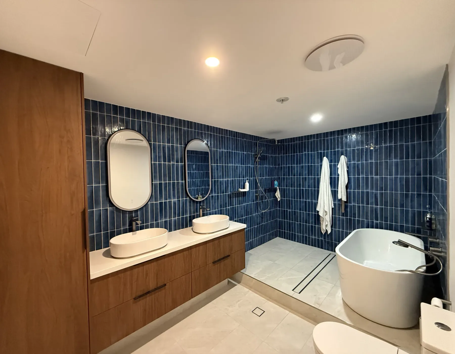 Premium bathroom renovation with a freestanding oval bath, dual backlit oval mirrors and navy feature tiling